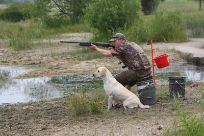 A man pointing a shotgun with a dog sitting next to him.